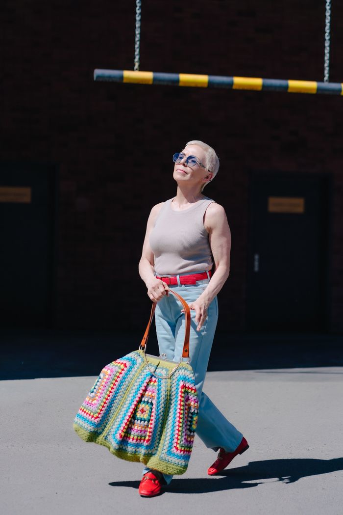Stylish senior woman carrying a colorful crochet bag, walking outdoors on a sunny day.